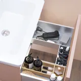 Stilfull badrumsinspiration med beige tvättställsskåp med innerskiva, överskåp, öppen hylla, ovalt spegel med belysning, matchande pendellampor, hylla under spegeln och vägghängd toalett. Väggar med ljusa, avlånga kakelplattor