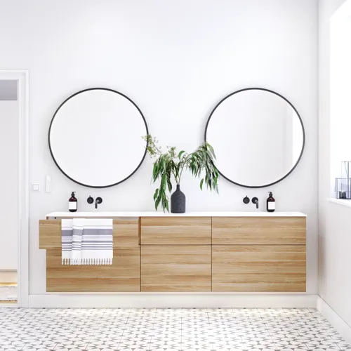 Nordiskt badrum i trä med vackra runda speglar med svarta kanter och gott om förvaring i badrumsmöblerna