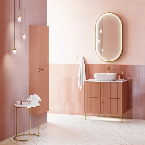 Stor vintage badrum med terrakottafärgat tvättställsskåp, bordstående handfat, ovalt spegel med mässingskant, ljusrosa och grå plattor ger ett romantiskt, feminint utseende