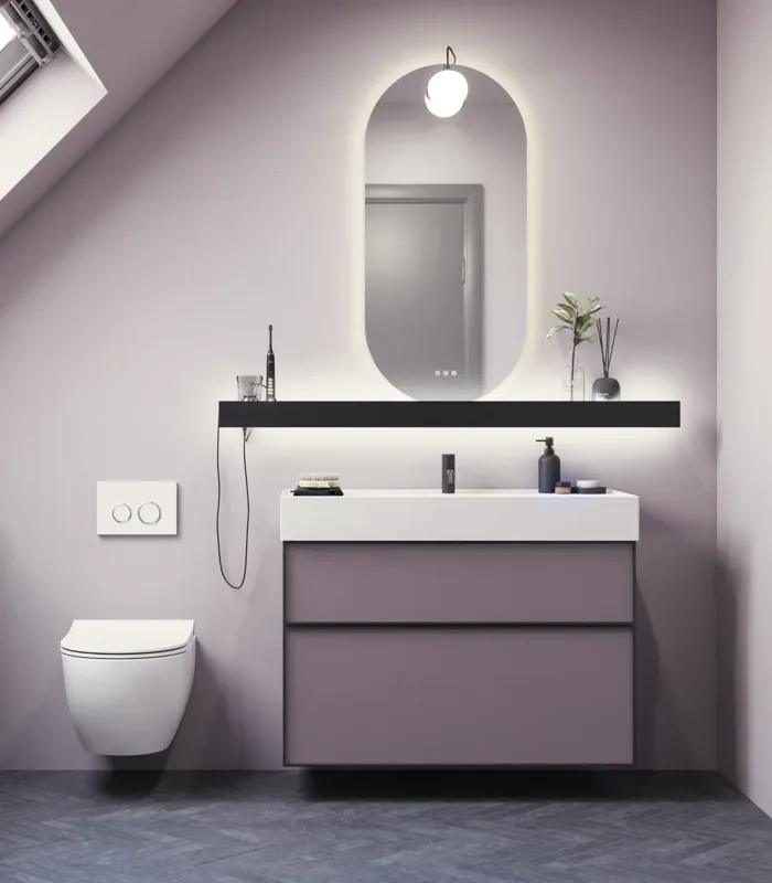 Badrum med snedtak inspiration, med badrumsmöbler i lila med eleganta ramfronter, vacker oval spegel med lampa, snygg och praktisk hylla, samt lilamålad vägg och grått fiskbensgolv som ger ett elegant och modernt uttryck.