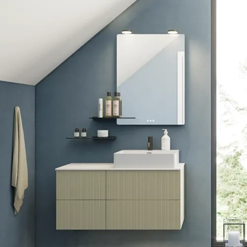 Badrum med snett tak inspiration, beige badrumsmöbler med räfflor, elegant bänkskiva och fyrkantigt bordsmonterat handfat, vacker fyrkantig spegel med stilfulla hyllor, blå väggar, stora fönster och svart fiskbensgolv ger ett ljust och urbant utseende.