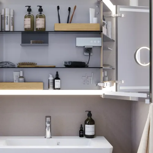 Liten badrumsinspiration med tvättställsskåp och överskåp över toalett i beige specialfärg, elegant spegelskåp med integrerat ljus, de ljusa färgerna och vita gardinen skapar en romantisk och feminin atmosfär.