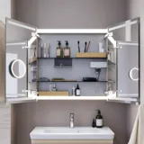 Liten badrumsinspiration med tvättställsskåp och överskåp över toalett i beige specialfärg, elegant spegelskåp med integrerat ljus, de ljusa färgerna och vita gardinen skapar en romantisk och feminin atmosfär.