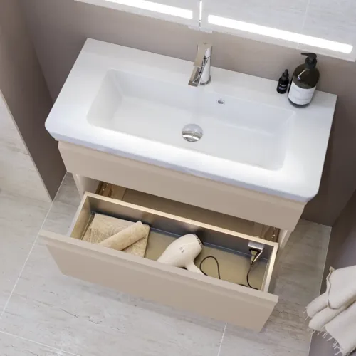Liten badrumsinspiration med tvättställsskåp och överskåp över toalett i beige specialfärg, elegant spegelskåp med integrerat ljus, de ljusa färgerna och vita gardinen skapar en romantisk och feminin atmosfär.