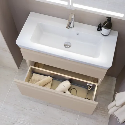 Liten badrumsinspiration med tvättställsskåp och överskåp över toalett i beige specialfärg, elegant spegelskåp med integrerat ljus, de ljusa färgerna och vita gardinen skapar en romantisk och feminin atmosfär.