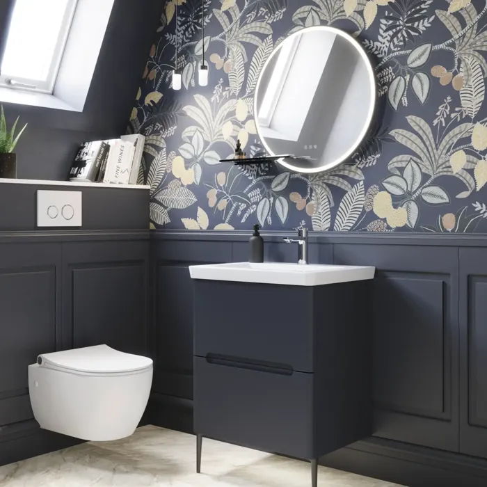 Badrumsinspiration med mörkblå väggpaneler, romantisk blommig tapet, mörkblått tvättställsskåp med mjuka former och en vacker rund spegel med ljus som skapar en vintagekänsla
