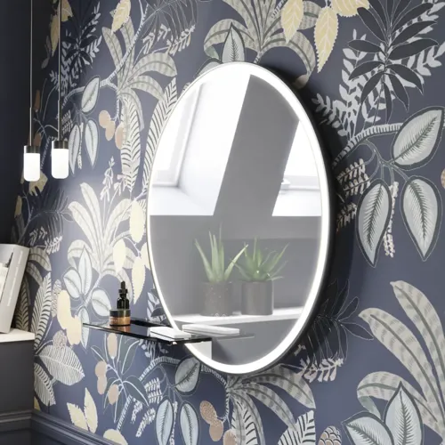 Badrumsinspiration med mörkblå väggpaneler, romantisk blommig tapet, mörkblått tvättställsskåp med mjuka former och en vacker rund spegel med ljus som skapar en vintagekänsla