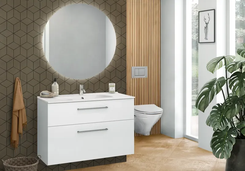 Minimalistiskt vitt tvättställsskåp med djup bottenlåda och kromhandtag, elegant runt spegel med ljus samt moderna plattor som ger en stilren estetik.