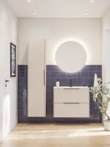 Badrumsinspiration med avlångt blått kakel, elegant beige underskåp och högskåp med svarta, minimalistiska och avlånga handtag samt en rund spegel med ljus för en vacker och kontrasterande look.