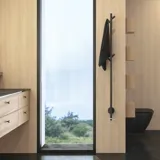 Stilrent badrum i skandinavisk och japandi inredningsstil med ljusa träväggar, rund spegel och minimalistiska badrumsmöbler.