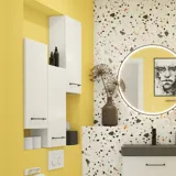 Liten badrumsinspiration med vitt tvättställsskåp med svart handtag och svart elegant handfat, vacker rund spegel med svart kant, förskjutna överskåp samt terrazzo vägg och golv och gula väggar ger ett modigt och modernt utseende.