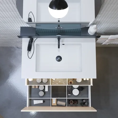 Stilfull badrumsinspiration med beige tvättställsskåp med innerskiva, överskåp, öppen hylla, ovalt spegel med belysning, matchande pendellampor, hylla under spegeln och vägghängd toalett. Väggar med ljusa, avlånga kakelplattor.