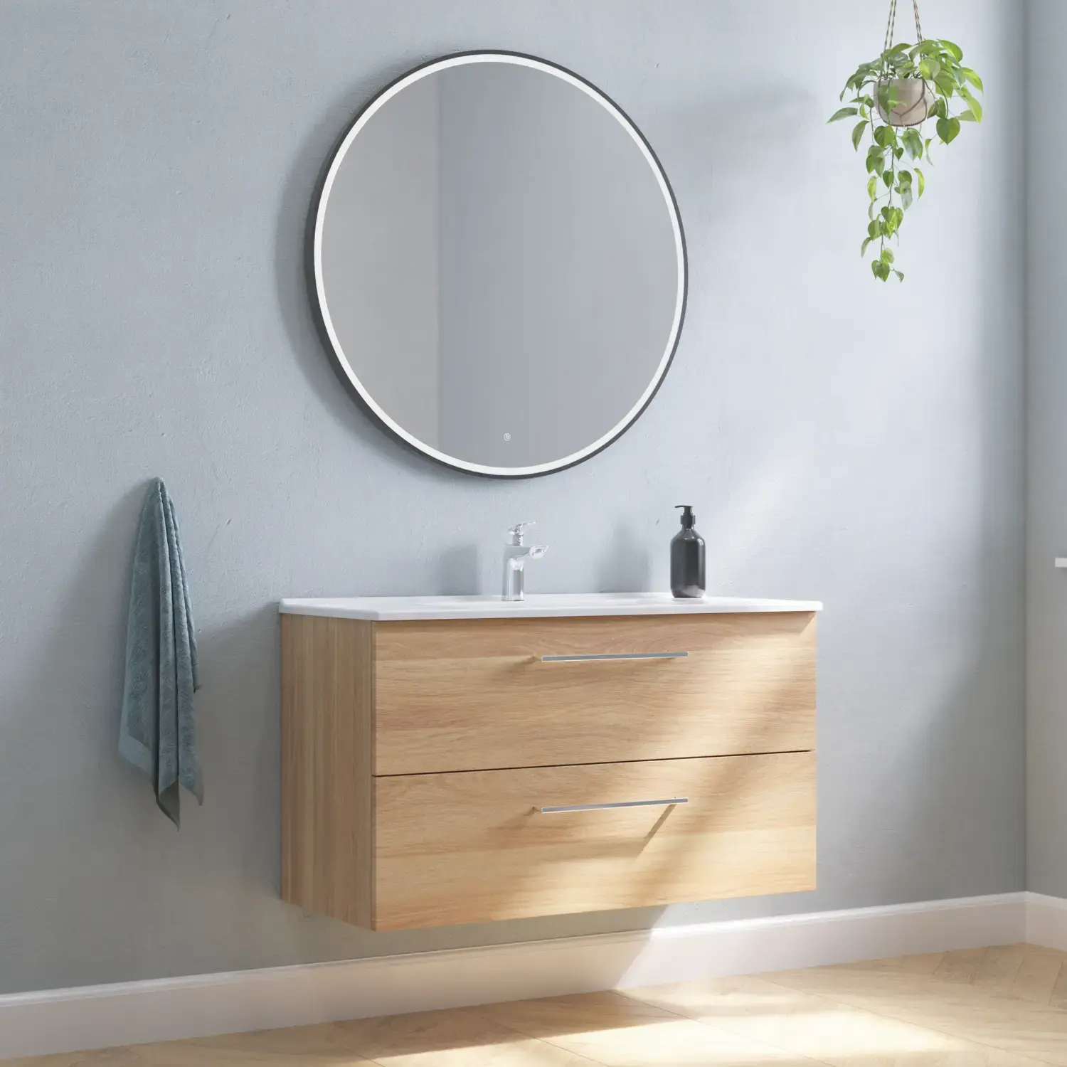 Stor badrumsinredning med underskåp i Warm Oak med elegant tvättställ, kromade handtag och vacker rund spegel med svart kant och ljus, fiskbensparkett på golvet och grå väggar för en modern look.