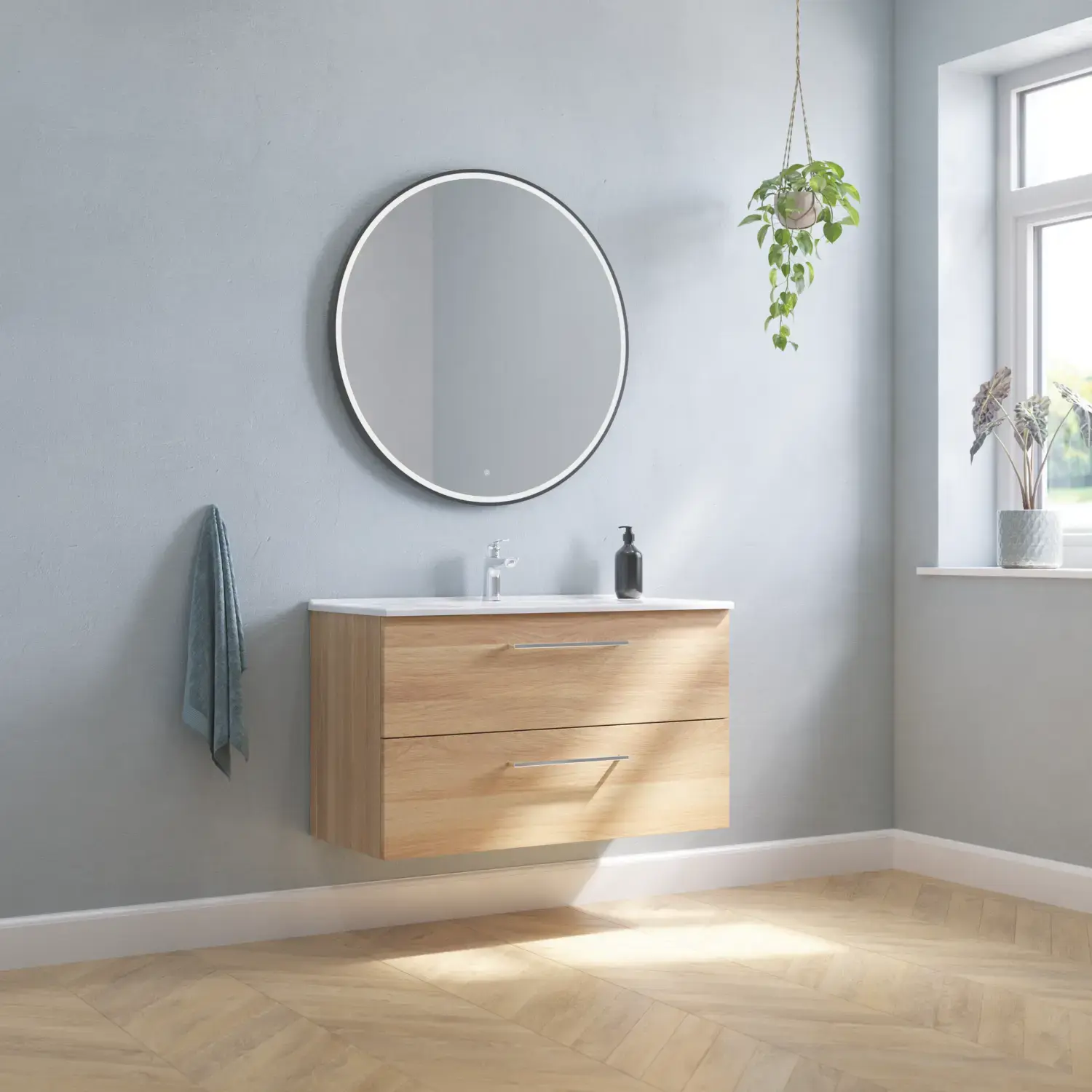 Stor badrumsinredning med underskåp i Warm Oak med elegant tvättställ, kromade handtag och vacker rund spegel med svart kant och ljus, fiskbensparkett på golvet och grå väggar för en modern look.