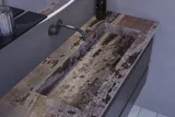 Stor badrumsinspiration med grå underskåp med integrerat handtag, snyggt sidomonterat handfat, fyrkantig spegel med rundade hörn, väggar i betonglook och råa material för en urban look