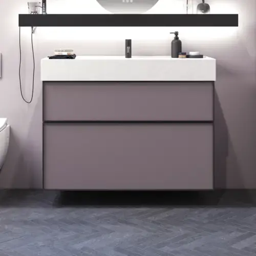 Badrum med snedtak inspiration, med badrumsmöbler i lila med eleganta ramfronter, vacker oval spegel med lampa, snygg och praktisk hylla, samt lilamålad vägg och grått fiskbensgolv som ger ett elegant och modernt uttryck.